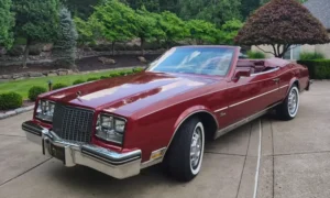 ביואיק ריביירה קבריולט 1983 בצבע בורדו יין עם גג פתוח – מבט מהצד על עיצוב ה-E-Body הקלאסי.