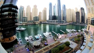 קו הרקיע של מרינה דובאי (Dubai Marina) עם גורדי שחקים מודרניים ומגדל קאיאן המפותל, מלווה בשייט מעבורת על המים, איחוד האמירויות הערביות.