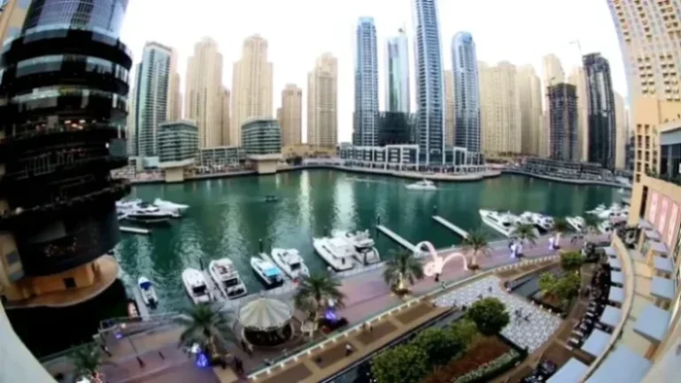 קו הרקיע של מרינה דובאי (Dubai Marina) עם גורדי שחקים מודרניים ומגדל קאיאן המפותל, מלווה בשייט מעבורת על המים, איחוד האמירויות הערביות.