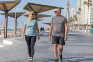 גבר ואישה בשנות ה-60 הולכים בטיילת תל אביב לצד הים עם סככות הצללה ברקע